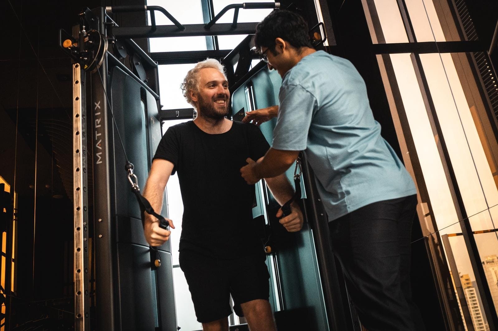 Personal trainer guiding a client through a cable machine exercise in a Bangkok gym