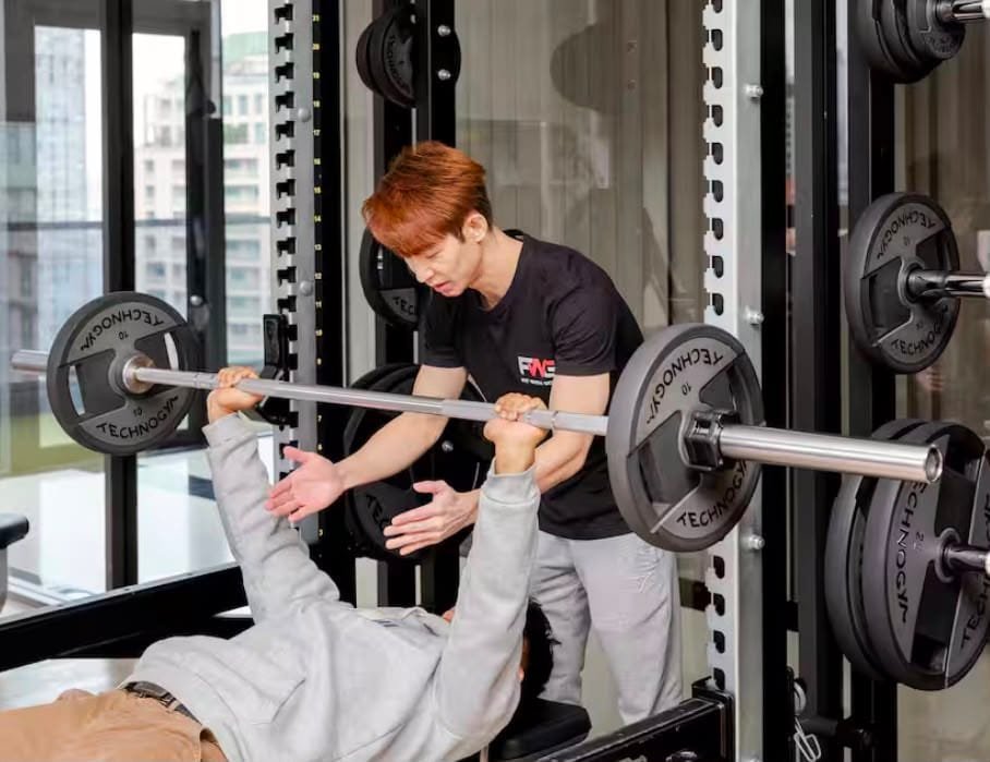 Coach spotting a client on a barbell bench press during partner personal training in Bangkok