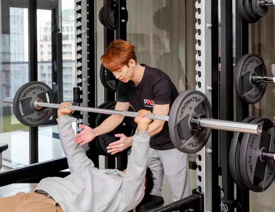 Coach spotting a client on a barbell bench press during partner personal training in Bangkok