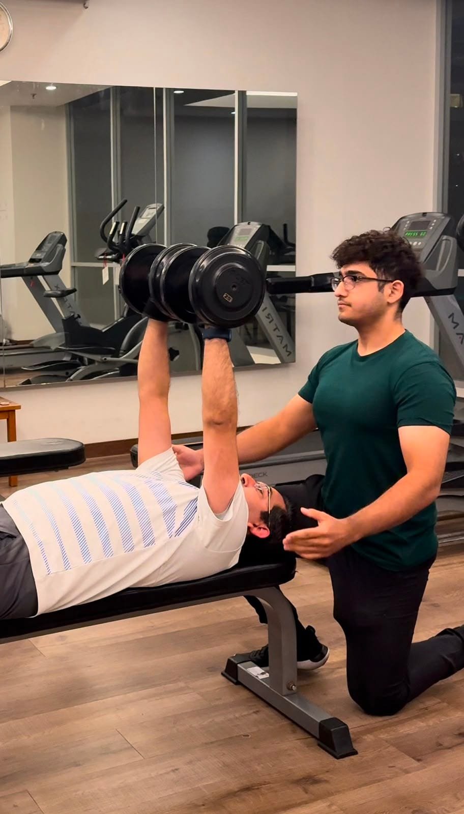 Personal trainer spotting a client during a dumbbell chest press in a private gym