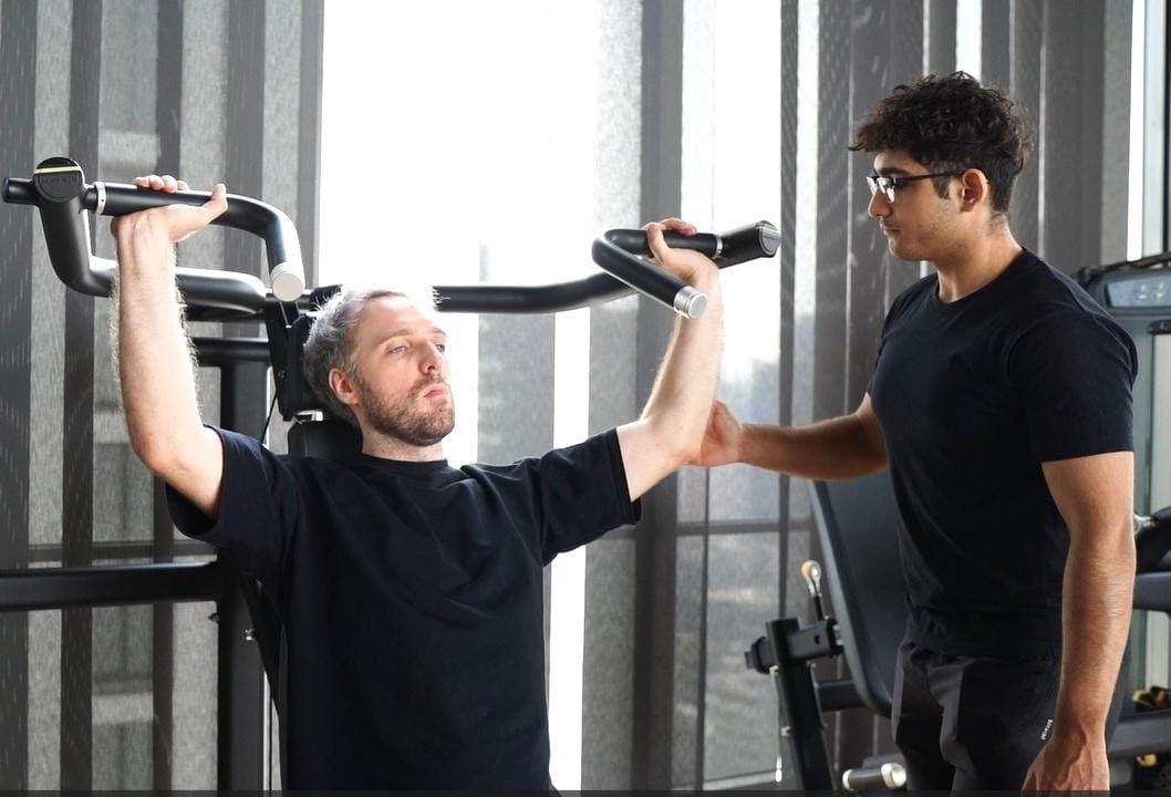 Trainer guiding a client's shoulder press form as part of a nutrition guide for personal training program